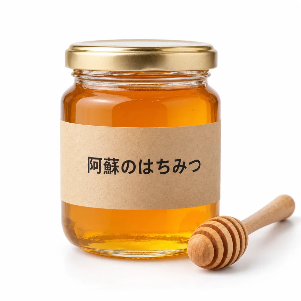 白背景で撮ったような、ラベルに「阿蘇のはちみつ」と書かれたはちみつの瓶と木のスプーンの商品写真